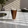 Tall transparent double wall coffee glass filled with brown milk coffee and a light foam layer