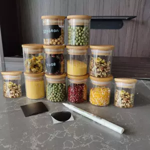 Set of clear glass storage jars with natural bamboo lids and black chalkboard labels for pantry organization.