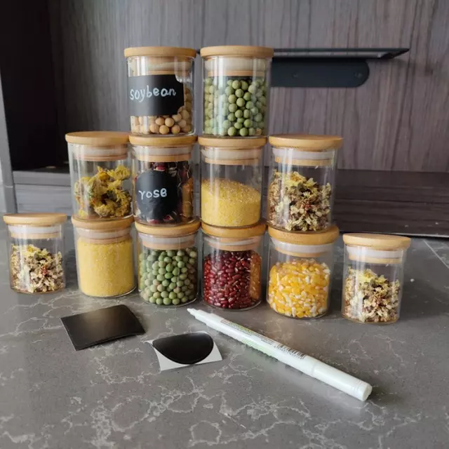 Set of clear glass storage jars with natural bamboo lids and black chalkboard labels for pantry organization.