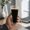 Transparent narrow waist double wall coffee glass filled with dark coffee and golden crema