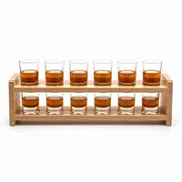 Twelve clear whiskey shot glasses displayed on a two-tier wooden rack